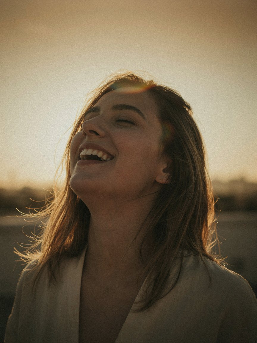 A woman laughing with her head tipped back, low sun blazing through her hair