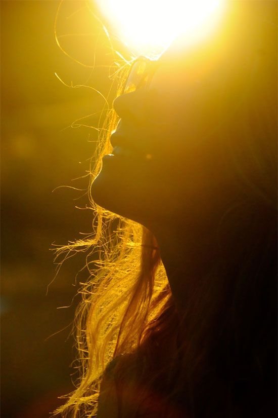 A woman's face lifted into low golden sunlight, her hair lit from behind