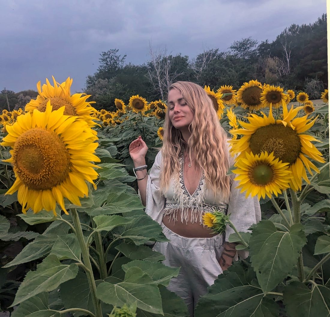 Maia standing among tall sunflowers with her eyes closed